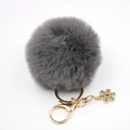 Détail du porte-clés pompon gris en fausse fourrure avec fermoir doré et flocon vert - Gris clair