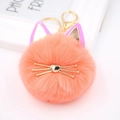 Close-up of cute peach cat faux fur pompom keychain with gold whiskers and heart nose - Orange Red
