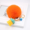 Detail of orange fluffy pompom keychain with yellow pineapple charm and blue bell - Orange