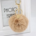 Detail van een lichtbruine pluche pompon sleutelhanger met gouden sneeuwvlok hanger goud - Khaki