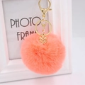 Detail view of coral orange plush ball keychain with golden snowflake charm and hardware - Orange Red