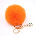 Détail d'un porte-clés pompon orange avec charme de sapin de Noël et attache dorée - Orange