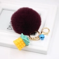 Detail of burgundy faux fur pompom keychain with yellow silicone pineapple and blue bell charm - Purplish Red