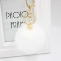Detailed macro view of white plush pompom keychain with golden metal snowflake charm - White