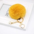 Detail view of yellow faux fur pompom keychain with gold lobster clasp and pearl accent - Orange
