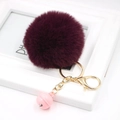 Macro detail of plush purple faux fur ball keychain with golden clasp and pink bell charm - Fuschia