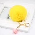 Close-up of bright yellow faux fur pompom keychain with golden clasp and pink bell - Yellow