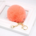 Close-up of pink fluffy pompom keychain with gold lobster clasp and white pearl detail - Orange Red