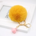 Close-up of fluffy yellow faux fur pompom keychain with golden ring and pink bell - Orange