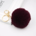 Close-up of fluffy burgundy faux rabbit fur pom pom with a golden metal keychain clasp - Purplish Red