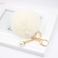 Gros plan d'un porte-clés pompon blanc doux avec détails dorés et perle élégante - Blanc Cassé
