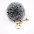 Gros plan d'un porte-clés pompon gris avec pendentif flocon vert et fermoir mousqueton doré - Noir bicolore