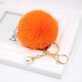 Detail of an orange faux fur keychain with a gold chain and white pearl accent - Orange
