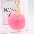 Close-up of pink fluffy pompom keychain with golden metal snowflake pendant and lobster clasp - Watermelon red