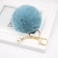 Macro shot of light blue faux fur pompom keychain with white pearl and gold metal hardware - Teal