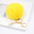 Detail of fluffy yellow faux fur pompom keychain with gold clasp and pearl charm decoration - Yellow