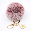 Gros plan du porte-clés pompon en peluche rose avec anneau doré et breloque marguerite - Rouge bicolore