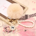 Détail du porte-clés pompon en fausse fourrure beige avec bracelet perle et nœud doré - Noeud de Perles / Nu
