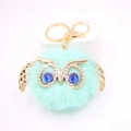 Détail du porte-clés pompon chouette bleu Tiffany avec des ailes dorées et des yeux en gemme - Porte-clés Doré / Vert menthe