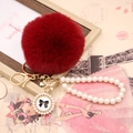 Detailed close-up of dark red faux fur pompom with golden bow and pearl chain strap - Pearl Bowknot / Burgundy