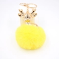 Détail de la breloque tête de cerf dorée avec un pompon en fausse fourrure jaune doux - Jaune