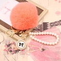 Detail of coral faux fur pompom keychain with white pearl chain and golden number 5 bow charm - Pearl Bowknot / Orange Red