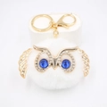 Détail d'un porte-clés hibou en peluche blanche avec finitions dorées et yeux bleus - Porte-clés Doré / Blanc
