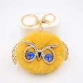 Gros plan d'un porte-clés hibou jaune duveteux avec ailes dorées et yeux bleu cristal - Porte-clés Doré / Orange