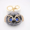 Détail du porte-clés chouette en fourrure avec yeux bleus et ailes en métal doré - Porte-clés Doré / Noir bicolore