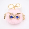 Détail d'un porte-clés hibou rose en fourrure avec ailes dorées et yeux bleus brillants - Porte-clés Doré / Rose Clair