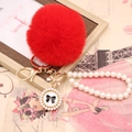 Détail d'un porte-clés en fausse fourrure rouge avec sangle en perles et pendentif nœud - Noeud de Perles / Rouge