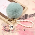 Detail view of a mint green faux fur pompom with a pearl wrist chain and golden bow charm - Pearl Bowknot / Matcha Green