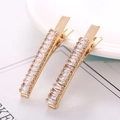 Detailed close-up of a pair of gold-plated alligator hair clips with baguette zircon stones - Gold Single Row Rectangular