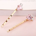 Detail von zwei goldenen Haarspangen mit rosa Herzkristallen und Strass auf weißen Seiten - Rosa