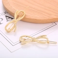 Dettaglio di fermagli per capelli dorati a forma di fiocco intrecciato lucido - Stile Fiocco Oro