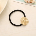 Elastic black hair tie with gold textured metal disk ornament on wooden background - Straw Hat
