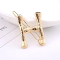 Macro detail of gold-plated H-letter hair clip with hammered metal texture design - Letter H