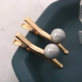 Détail de deux pinces à cheveux dorées ondulées avec perles grises sur plateau vert - Style 10 / Gris