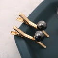 Vue macro de barrettes dorées avec perles gris foncé sur un plateau en céramique - Style 10 / Noir