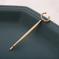 Détail d'une pince à cheveux dorée avec anneau texturé sur une assiette en céramique bleue - Lettre C