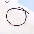 Nahaufnahme eines minimalistischen schwarzen Haargummis mit einer mattrosa herzförmigen Perle - Rosa