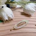 Vista dettagliata di un fermaglio ovale in resina bianco perla con accenti dorati - Ovale Bianco Perlato