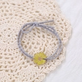 Detailed close-up of yellow daisy hair tie with grey elastic cord on lace mat - Lavender
