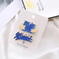 Detail view of two blue enamel cat pins with gold stars on white satin background - Blue Twin Jumping Cat Set