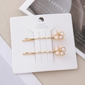 Details von zwei goldenen gewellten Haarspangen mit Perlenblumen auf dekorativer Karte - Irisierendes Weiß 5-Blatt Haarnadel Paar