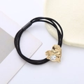 Close-up of triple-strand black hair tie with gold heart-shaped lava crystal detail - Iridescent White