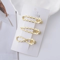 Gros plan de trois pinces à cheveux en métal doré avec texture torsadée sur carte blanche - Style Corde Géométrique Torsadée / Combinaison Or
