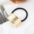 Nahaufnahme des goldenen Haargummis mit Metallstruktur und schwarzem Gummiband - Gold Plissierte Oberfläche