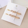 Détail de barrettes dorées élégantes avec cristaux roses sur carte de bijoux blanche - Café avec Nœud