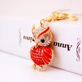 Golden owl keychain with red rhinestones and enamel details on white book background - Red